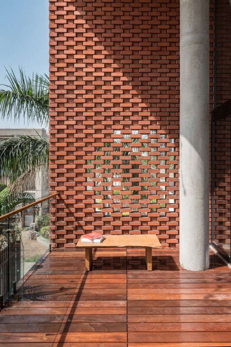 a wooden bench sitting on top of a wooden floor next to a brick wall and palm tree