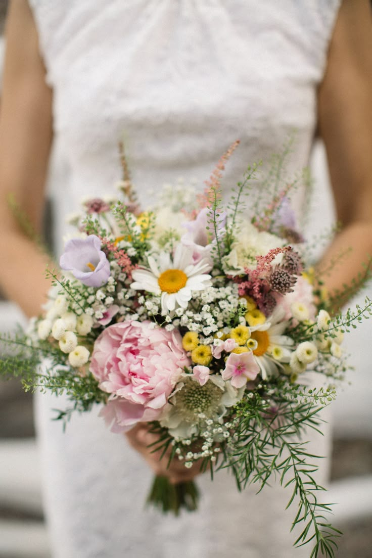 a woman holding a bouquet of flowers in her hands and wearing a white dress with lace