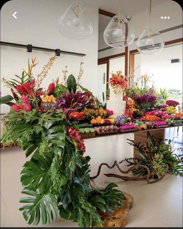 an arrangement of flowers and greenery on display in a room with hanging lights above