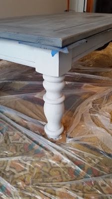 a white table sitting on top of a bed covered in plastic wrap and wood planks