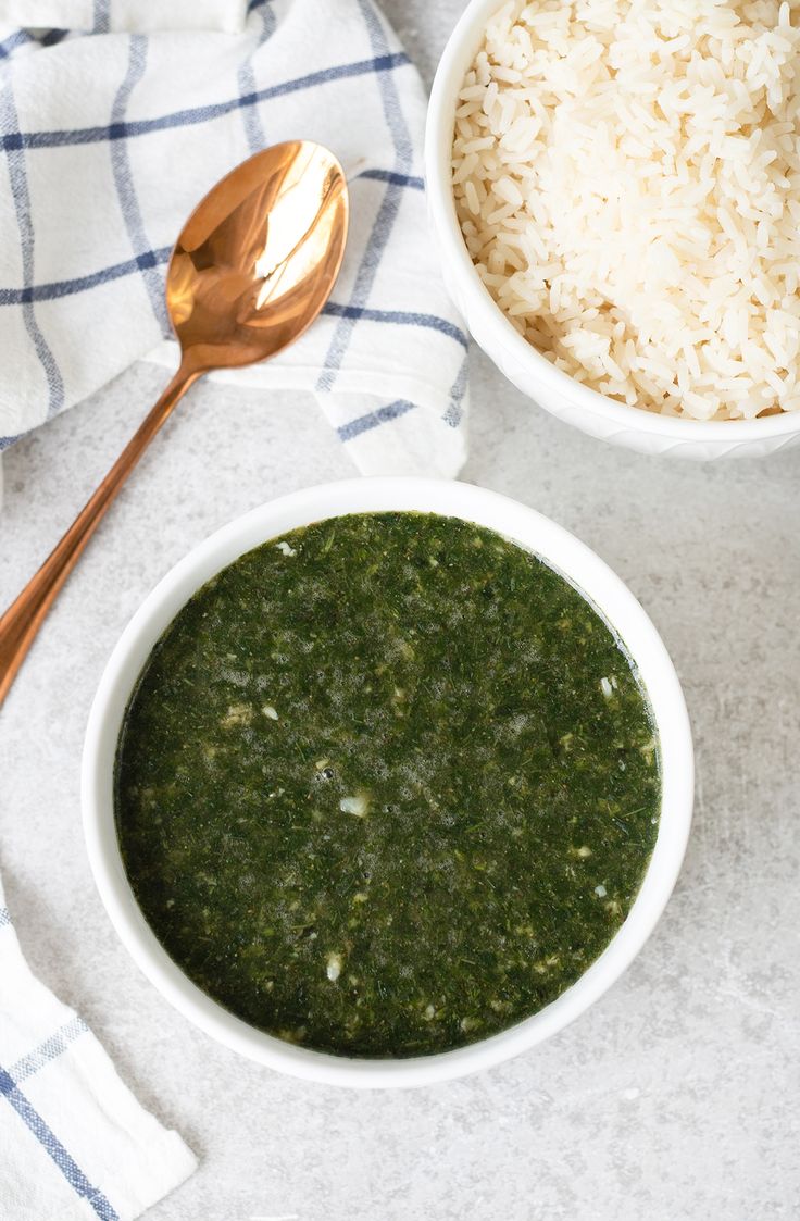 two white bowls filled with green food next to a spoon and bowl of rice on a table