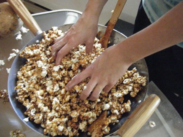 two hands reaching for popcorn in a pan