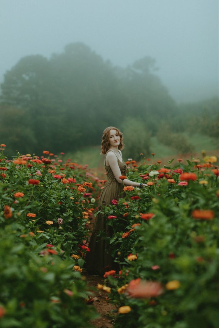 a woman standing in the middle of a field full of red and yellow flowers on a foggy day