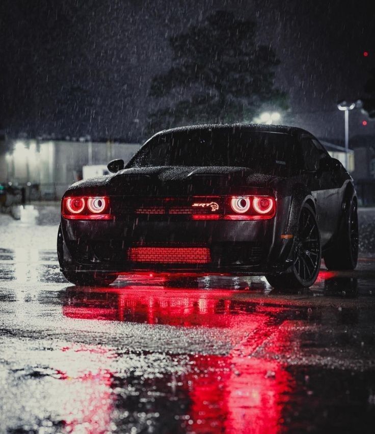 a black sports car parked on the side of a road in the rain at night