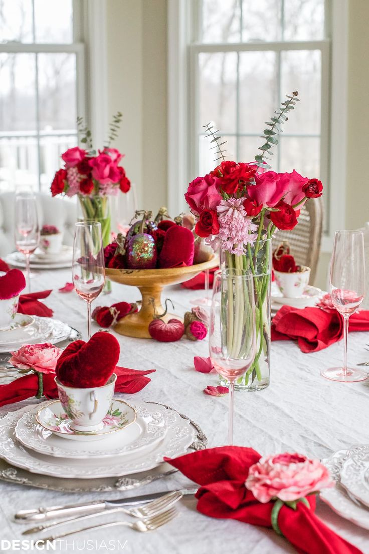 valentine's day table setting with red flowers in vases and napkins on the table