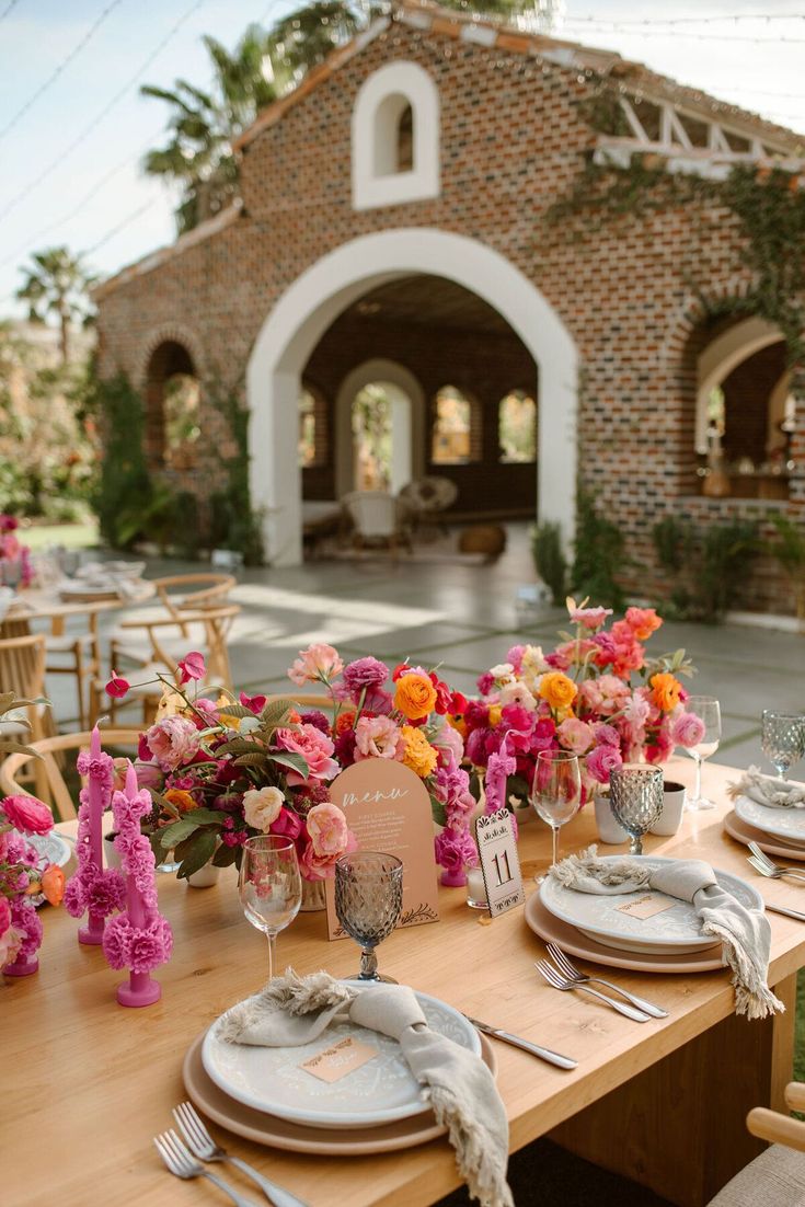 the table is set with pink and orange flowers in vases, napkins, and place settings