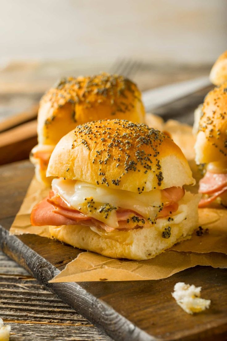 two ham and cheese sliders sitting on top of brown paper next to a knife