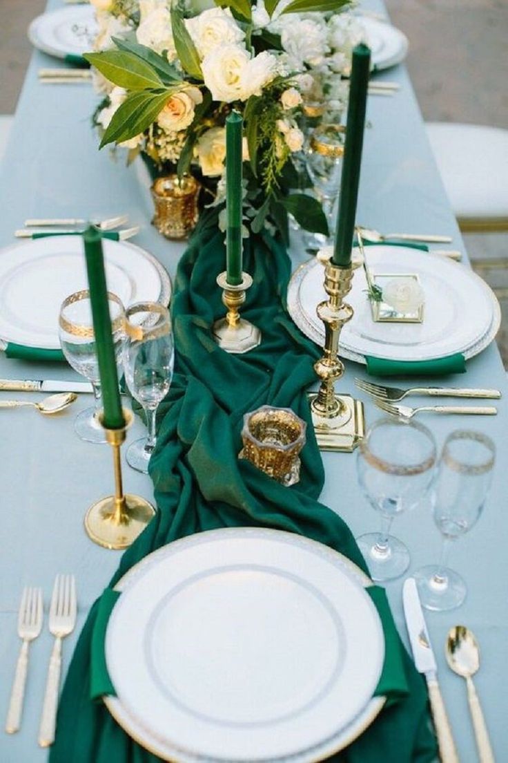 the table is set with white plates and green napkins, gold place settings and candles