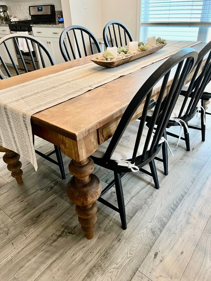 a wooden table with black chairs and a bowl of food on it's end