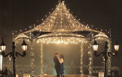 two people standing under a gazebo covered in christmas lights at night with one kissing the other