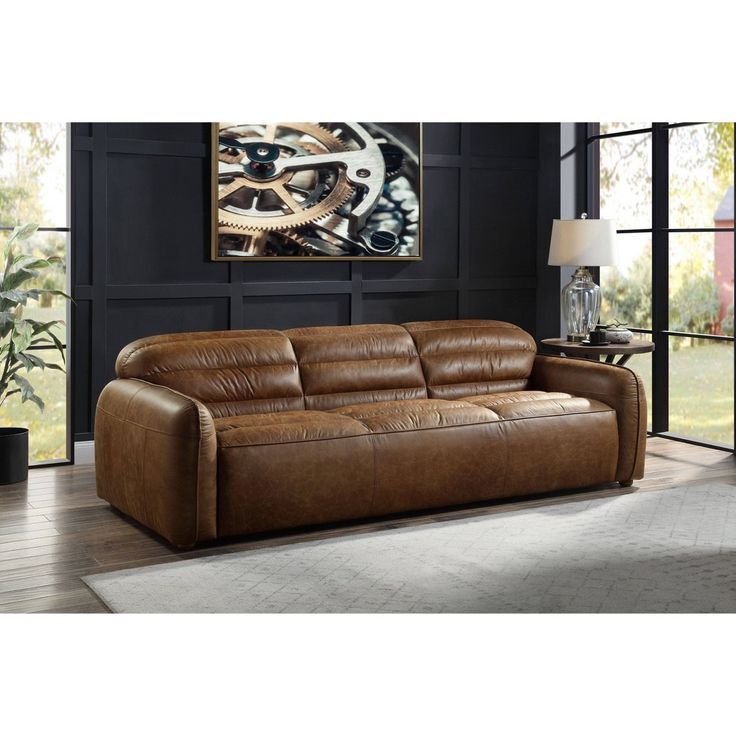 a brown leather couch sitting on top of a hard wood floor next to a window