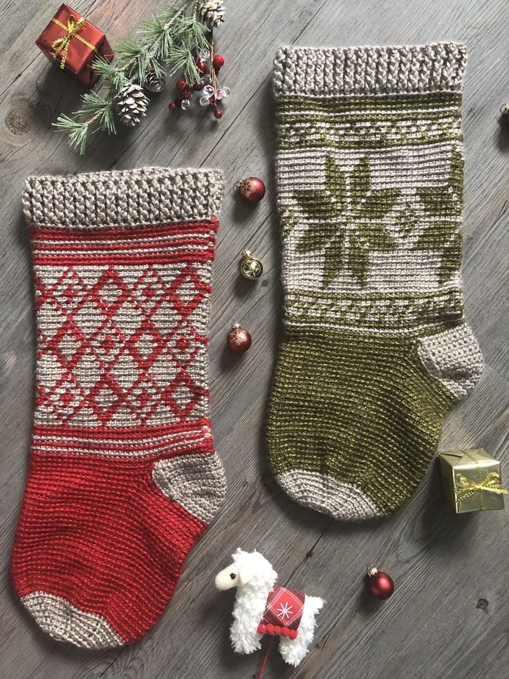 two knitted christmas stockings on a wooden floor next to ornaments and fir tree branches