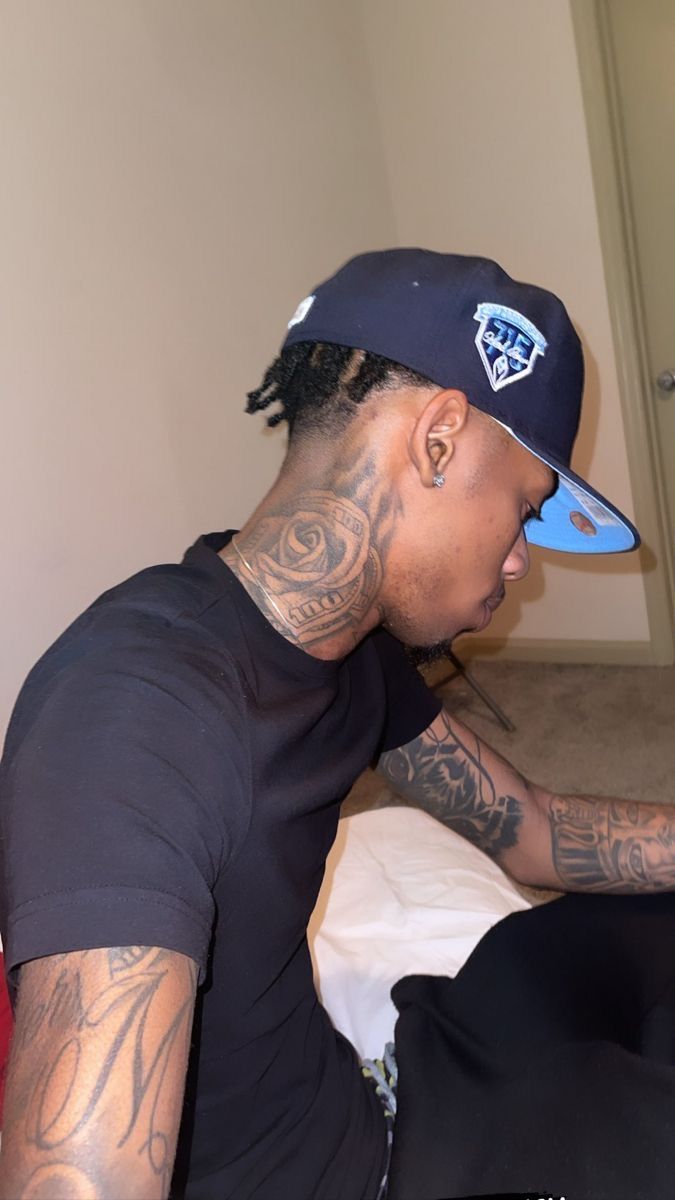 a man with tattoos on his arm sitting in front of a bed and looking at something