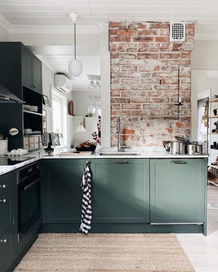 a kitchen with green cabinets and brick wall in the back ground, an area rug on the floor