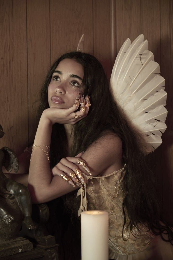 a woman with long hair and wings on her face posing for a photo next to a candle