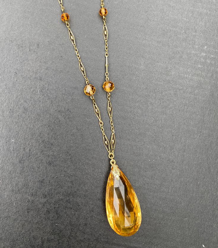 "A lovely Art Deco era 14K gold and citrine drop necklace. The citrine briolette drop is a sunny yellow color and measures an impressive 34 mm long by 17 mm wide by 11.4 mm deep. The many facets around the entire stone allows it to really shine. It has some natural inclusions as well as some minor surface abrasions as shown in the photos. The citrine is suspended from a delicate filigree necklace with citrine bead stations. Lovely open gold work on each gold panel. The clasp is stamped \"14K\" f Formal Amber Necklace With Large Pendant, Amber Necklace With Large Pendant For Formal Occasions, Amber Large Pendant Necklace For Formal Occasions, Vintage Briolette Necklace For Formal Occasions, Formal Amber Necklace In Fine Jewelry Style, Luxury Briolette Drop Necklace, Classic Teardrop Citrine Jewelry, Formal Faceted Briolette Necklaces, Formal Briolette Faceted Necklace