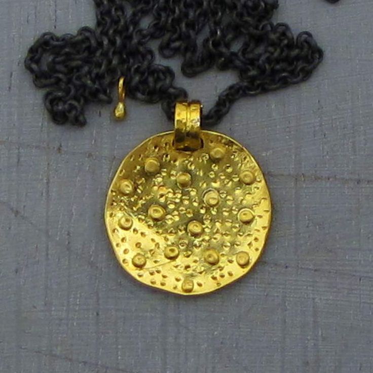 An exquisite solid gold necklace featuring a delicate handmade round 24k gold charm. This  pendant is adorned with hammered balls and gentle engravings, exuding a captivating "tribal" aesthetic with a textured allure that is truly unique. The chain of the necklace is made of oxidized silver, adding a touch of sophistication to the design. It is elegantly finished with a 14k gold hook clasp, ensuring both style and secure fastening. Pendant diameter - 0.7″ (17 mm). Chain length - 21.8″ (55.5 cm).  To enhance your gifting experience, the necklace will be thoughtfully packed in a gift box, The necklace will be shipped securely via DHL, typically taking 2-6 days to arrive. Should you have any inquiries or special requests, please do not hesitate to contact me. I am here to assist you and ensur Unique Gold Necklace With Coin Pendant, Hammered Yellow Gold Amulet Necklace, Yellow Gold Hammered Amulet Necklace, Gold Coin Necklace With Oxidized Finish, Handmade Yellow Gold Coin Amulet Necklace, Gold Hammered Pendant Necklace, Handmade Gold Coin Amulet Necklace, Handmade Yellow Gold Amulet Coin Necklace, Hammered Yellow Gold Round Disc Necklaces