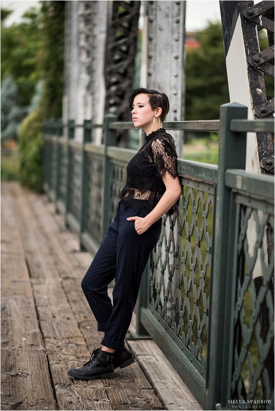 a woman standing on a bridge leaning against the railing with her hands in her pockets