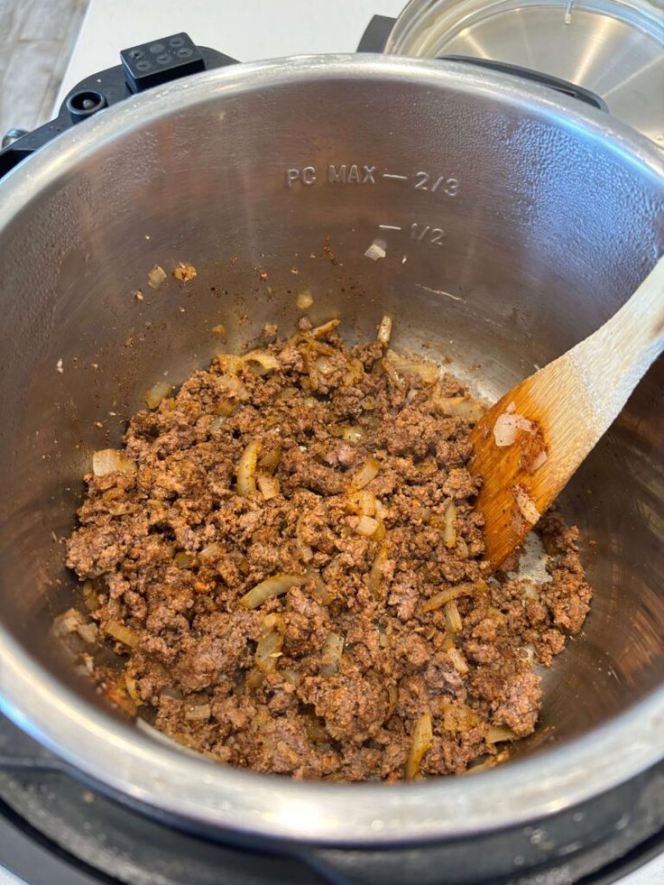 a wooden spoon in a pot filled with ground beef and onions on top of a stove