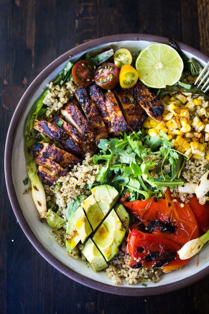 a bowl filled with meat, vegetables and rice on top of a wooden table next to a fork