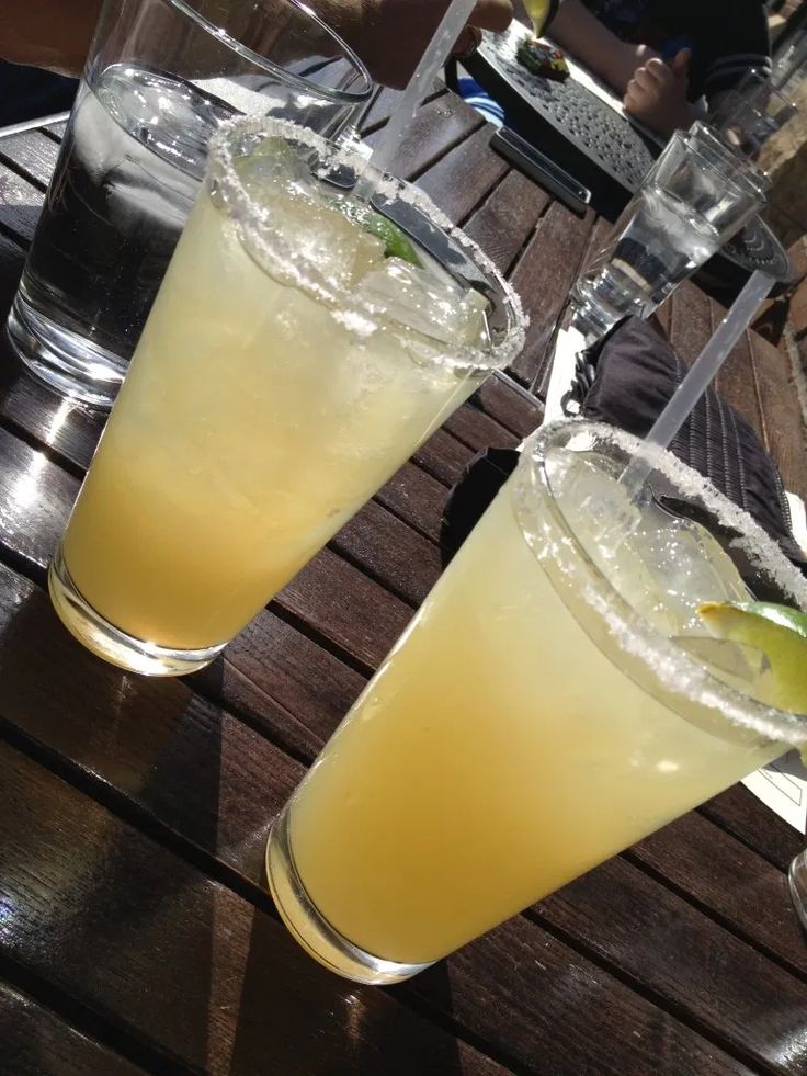 two glasses filled with drinks sitting on top of a wooden table next to each other