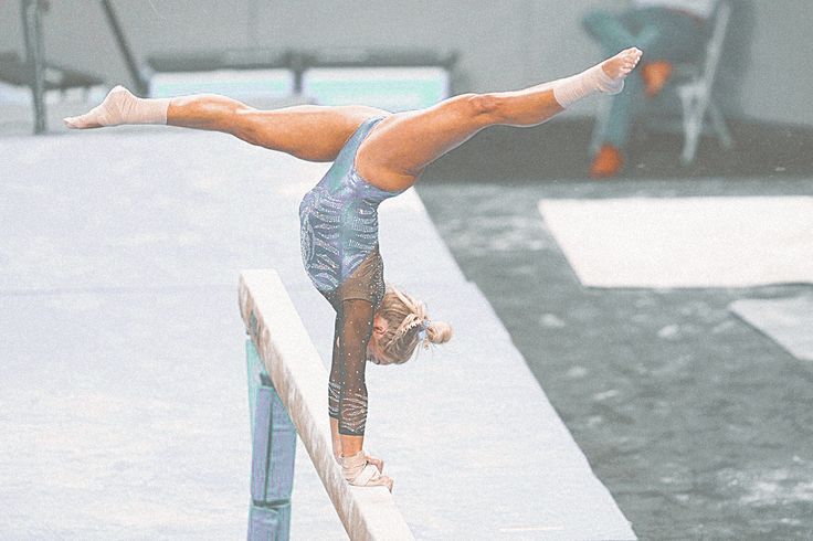 a woman doing a handstand on a beam in the middle of an outdoor area