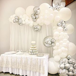 a white table topped with lots of silver and white balloons filled with confetti