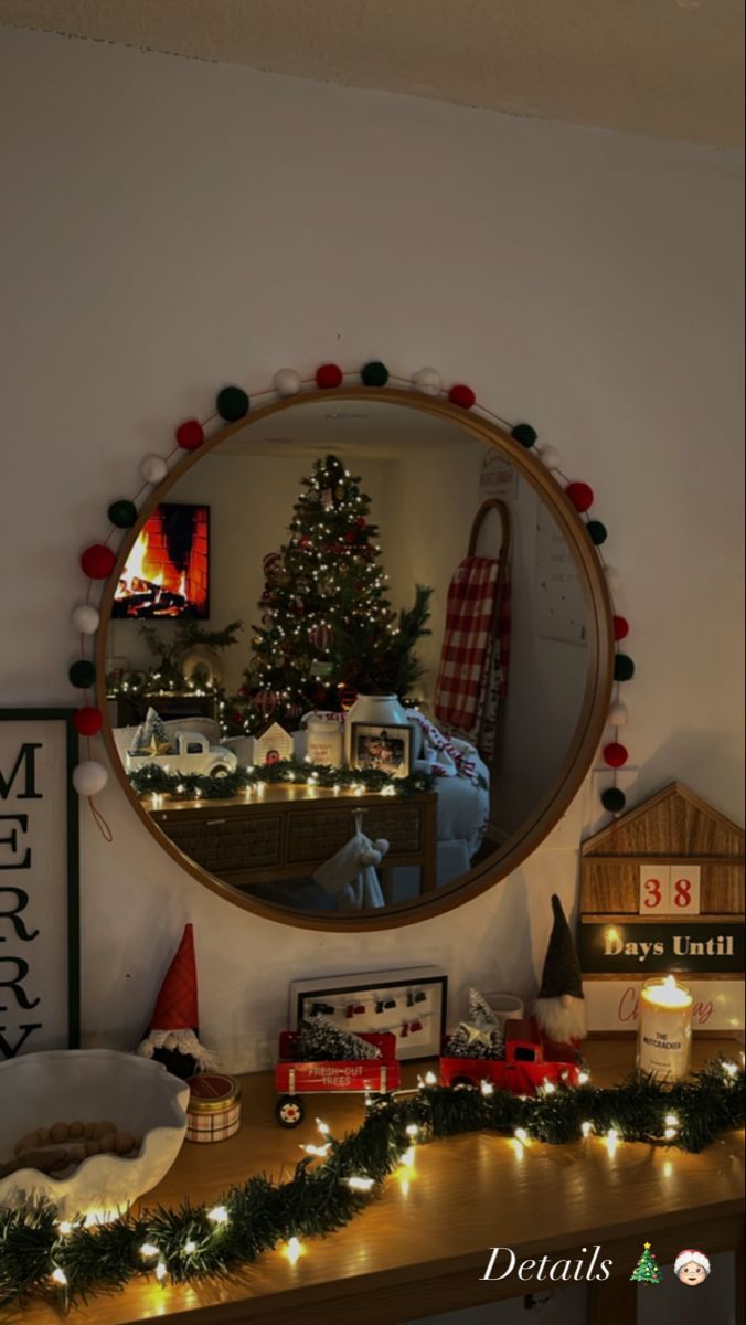 a christmas tree is reflected in a round mirror on a table with holiday decorations and lights around it