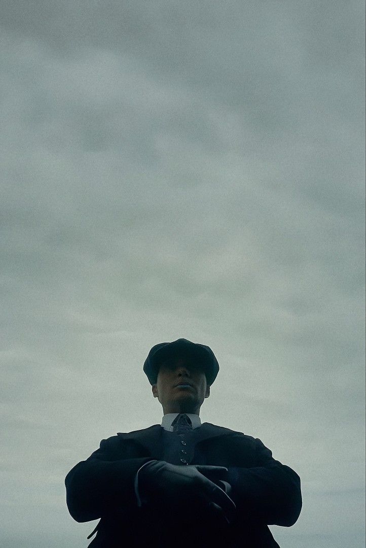 a man in a suit and hat standing with his arms crossed under an overcast sky