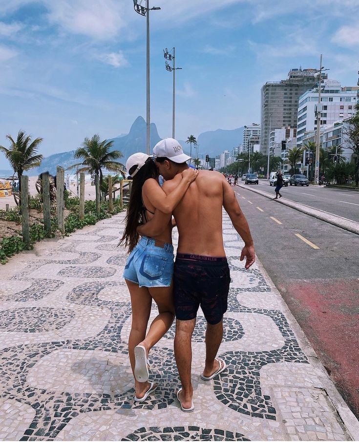 a man and woman walking down the sidewalk in front of some buildings with palm trees