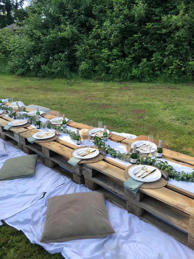 a long table set up with plates and napkins on it in the middle of a field