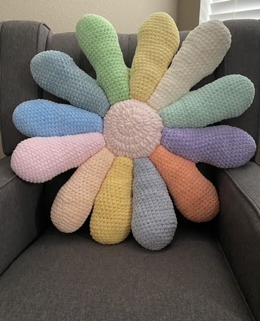 a crocheted flower pillow sitting on top of a gray couch next to a window