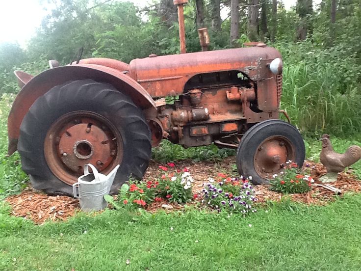 an old farm tractor sitting in the middle of a field with flowers and birds around it