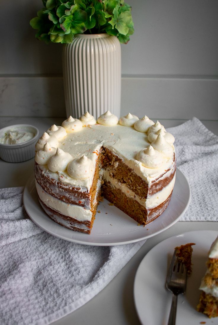 A carrot cake with two tiers and cream cheese frosting with a slice cut out of it. The slice is sitting on a plate next to the cake. Names On Cakes Ideas, Tiered Carrot Cake, Cute Carrot Cake Decorations, Cake Decorating Carrot Cake, Carrot Cake Wedding Cakes Simple, East Birthday Cakes, Carrot Cake Presentation, Easy Carrot Cake Decorating Ideas, Birthday Cake Carrot Cake