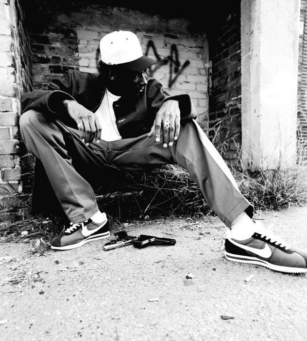 a black and white photo of a man sitting on the ground next to a brick wall