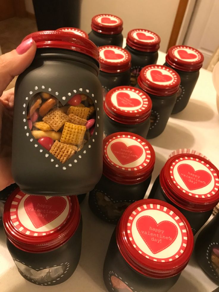 a person holding a jar filled with heart - shaped cookies and crackers in it