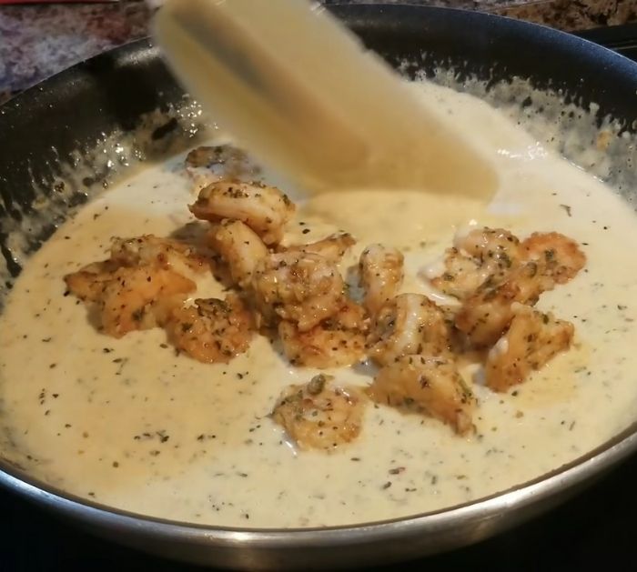 the sauce is being poured into the pan with some shrimp and cheese in it on the stove