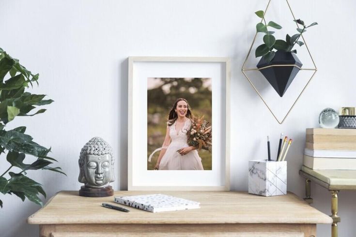 a white framed photograph sitting on top of a wooden table next to a potted plant