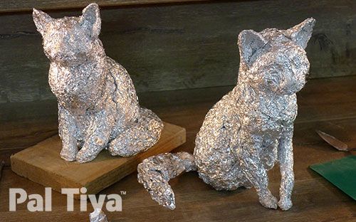 two tin foil cats sitting next to each other on a wooden table with knifes