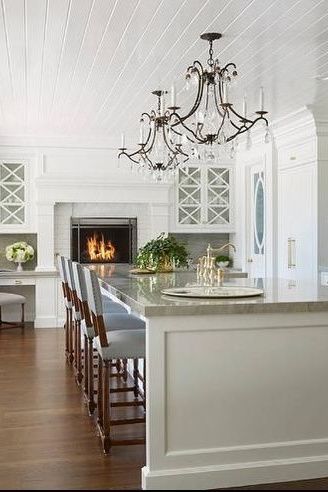 a large kitchen with white cabinets and an island in front of the fireplace is shown