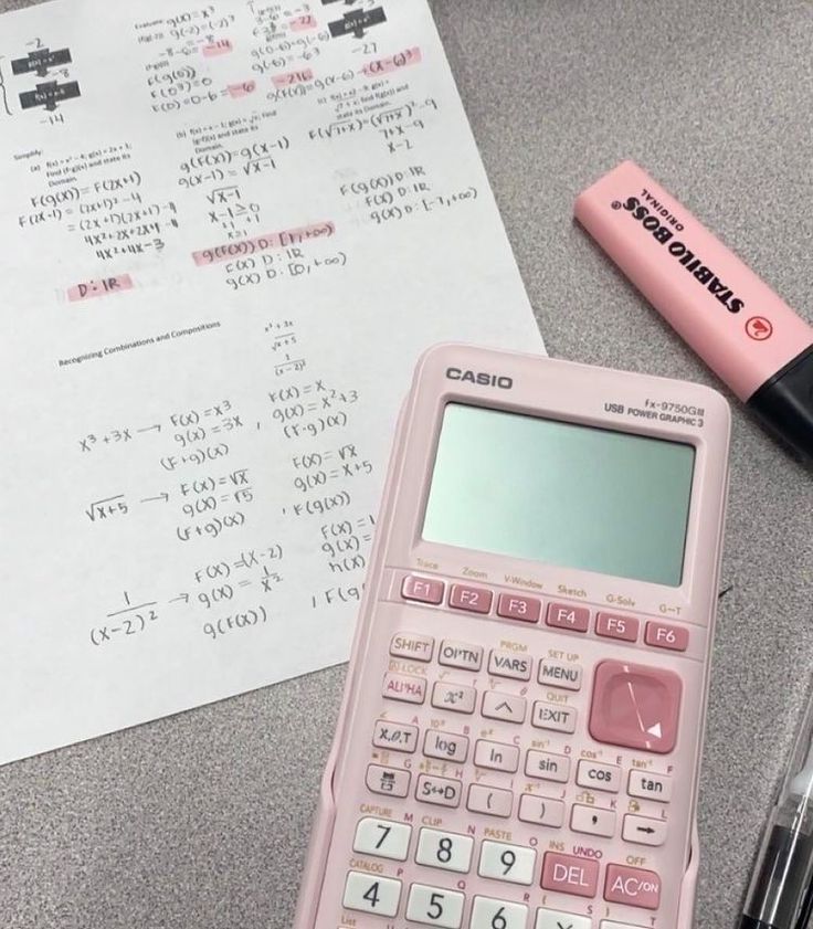 a pink calculator sitting on top of a table next to a pen and paper