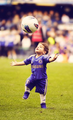 a young boy is playing with a soccer ball on the field in front of an audience