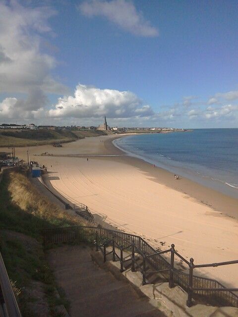 a sandy beach next to the ocean under a cloudy blue sky