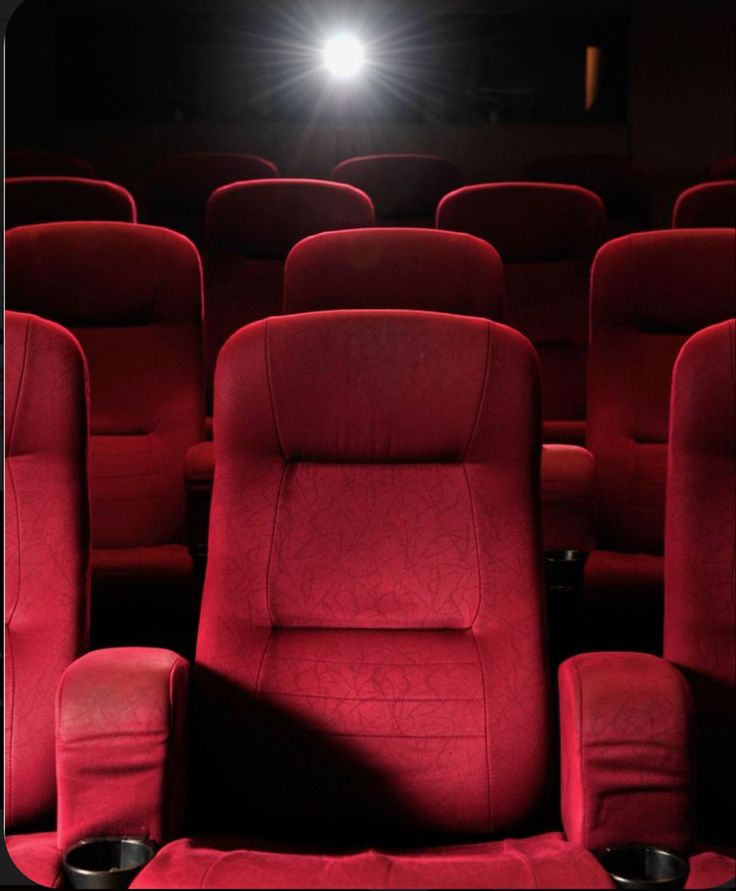 rows of red chairs in front of a projector screen with light shining on them