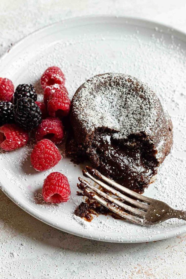 a white plate topped with a piece of chocolate cake next to raspberries and a fork