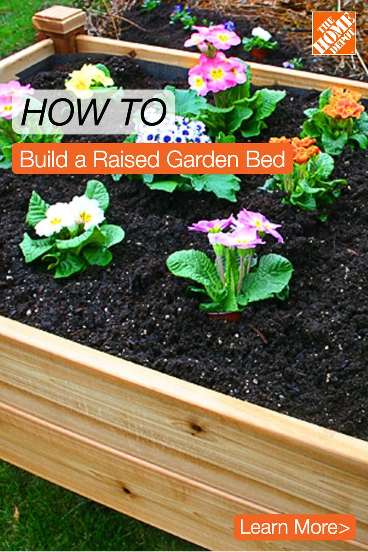 a raised garden bed with flowers and plants growing in the soil, on top of grass