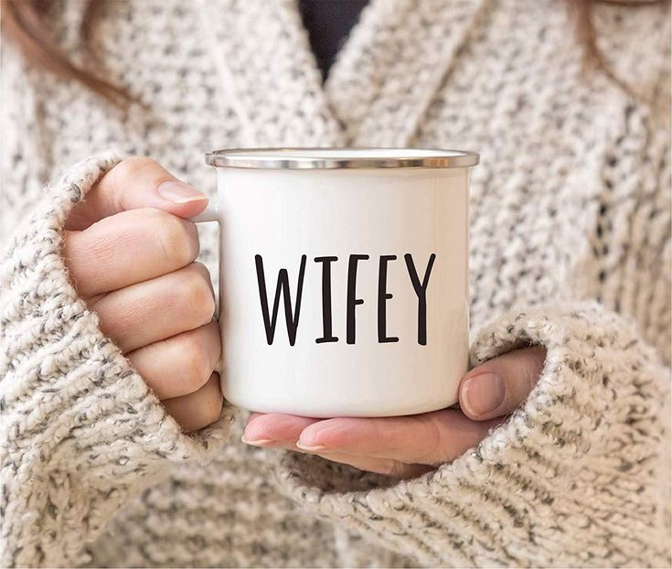 a woman holding a white coffee mug with the word autumn printed on it in black