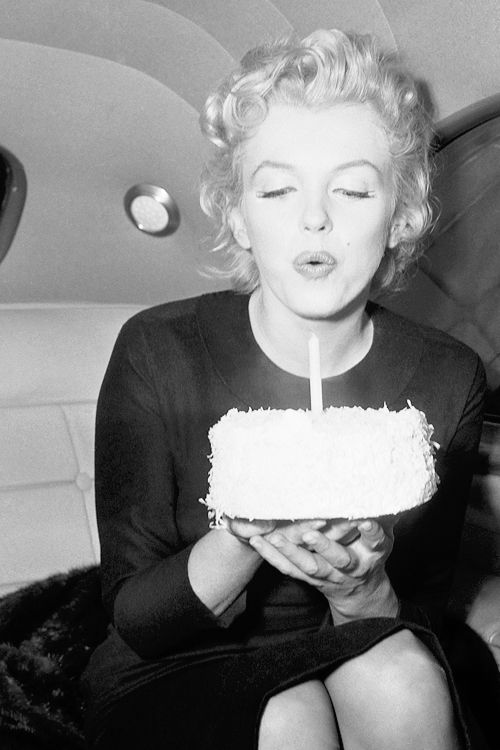 a woman sitting on an airplane with a cake in front of her and blowing the candles out