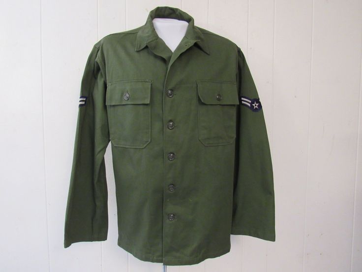 "Vintage 1960s U.S. Air Force military shirt. Made of green cotton. Has two chest patch pockets, button front, button cuffs and winged star patches on the shoulders. Size medium. Actual measurements are: 47\" at the chest 45.5\" at the waist 19.5\" shoulder seam to shoulder seam 24.5\" shoulder seam to cuff 30.5\" overall length In very good unused condition. New old stock. Has a small spot from storage(photo)." Retro Khaki Cotton Shirt, Green Military Style Button-up Shirt, Vintage Coveralls, Patches Vintage, 1950s Shirts, Air Force Military, Air Force Patches, Denim Coverall, Star Patches