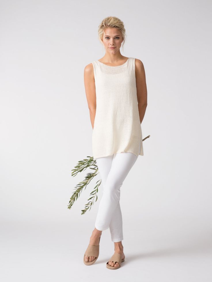 a woman in white pants and a tank top holding a green leafy twig